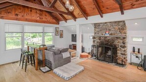 A spacious living room with a stone fireplace, wooden ceiling beams, and large windows. - Remodeled, Family-Friendly Home in Private Community on Candlewood Lake (New Fairfield)