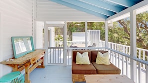 A covered porch with a wooden bench, a cushioned seating area with pillows, and a view of the backyard. - Gorgeous home in Wild Dunes with parking on Palm Blvd. (Isle of Palms)