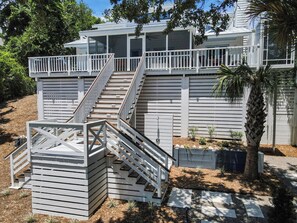 A modern house with a covered patio, a staircase leading to a deck, and a small garden area.