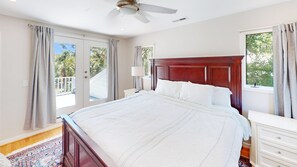 A spacious bedroom with a large bed, a wooden headboard, a nightstand, a lamp, and a view of the outdoors through the windows.