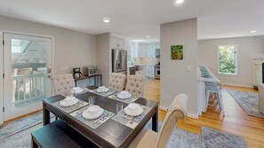 A modern kitchen with white cabinets, stainless steel appliances, and a dining area with a dark wooden table set for four.
