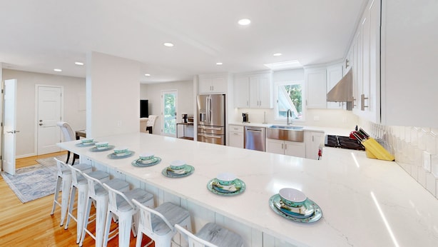A modern kitchen with white cabinetry, a large island with bar stools, stainless steel appliances, and a view of the outdoors. - Gorgeous home in Wild Dunes with parking on Palm Blvd. (Isle of Palms)