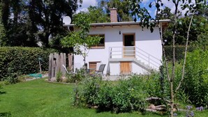 A white two-story house with a wooden deck and a small staircase leading to the entrance. - Gemütliches Ferienhaus im Grünen (Michendorf)