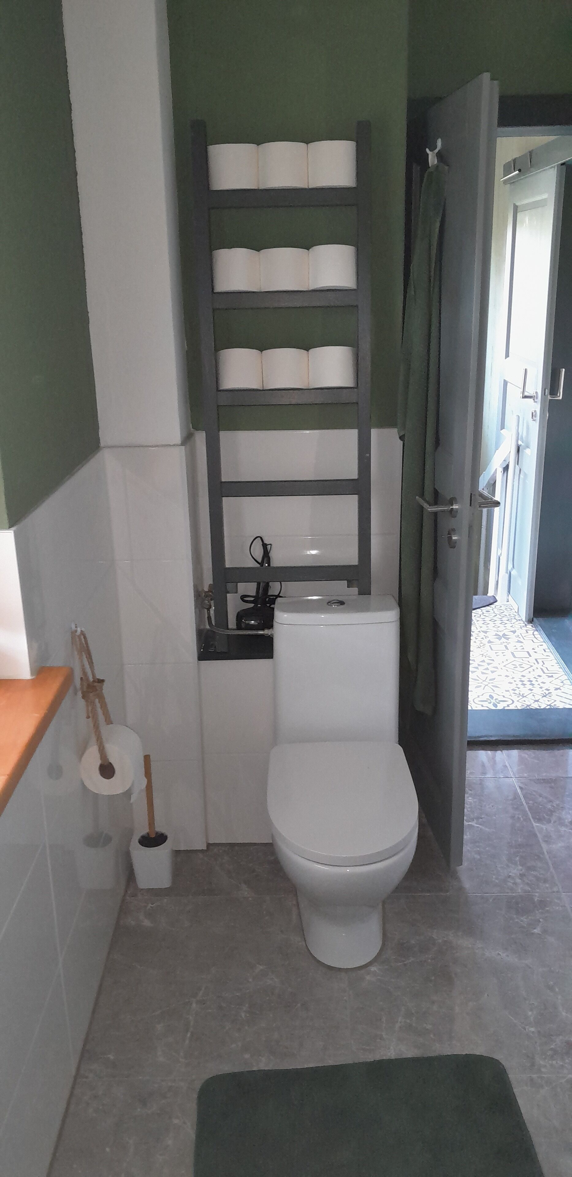 Un baño pequeño con inodoro, un estante con papel higiénico y cortina de ducha.