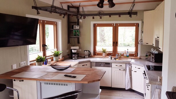 A kitchen with wooden countertops, white cabinets, a built-in dishwasher, and a large window providing natural light. - Gemütliches Ferienhaus im Grünen (Michendorf)