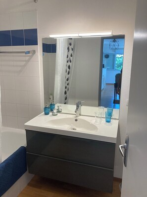 Bathroom features a large sink, mirror, and towel rack, with a shower curtain and wooden floor.