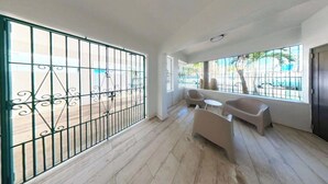 A room with a large window, a balcony with a metal railing, and a seating area with a sofa and two chairs.