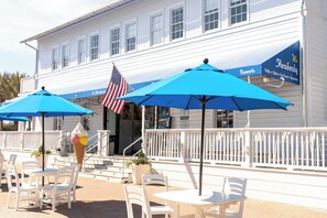 Un espace extérieur aménagé avec des chaises blanches et des parasols bleus, un grand cornet de glace et un drapeau américain.