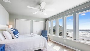 A bedroom with a bed, a ceiling fan, a chair, and large windows overlooking a beach. - Lost Colony is a beach front complex with a Community pool and pedestrian boardw (Port Aransas)