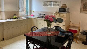 Una cocina funcional con estufa a gas, microondas y lavamanos. Hay una mesa de comedor con sillas y un florero con flores.