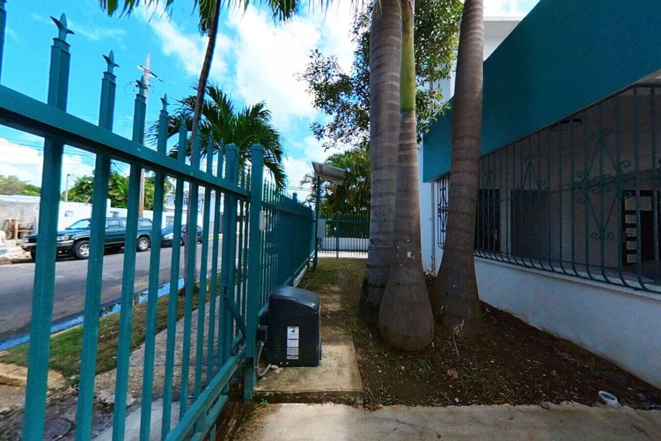 A gated residential area with a parked car, a mailbox, and a palm tree.