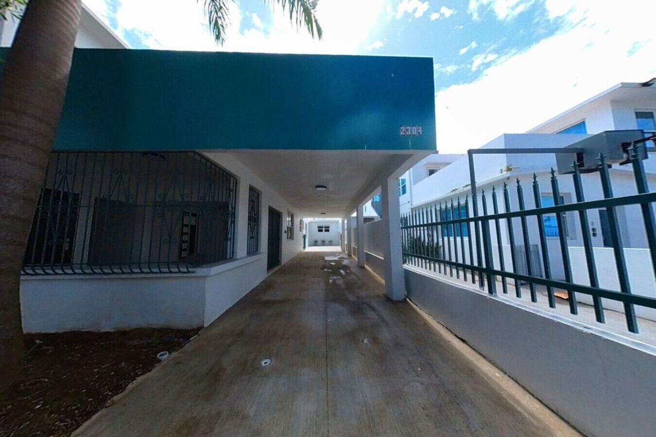 A covered walkway with a metal fence on one side and a building entrance on the other.