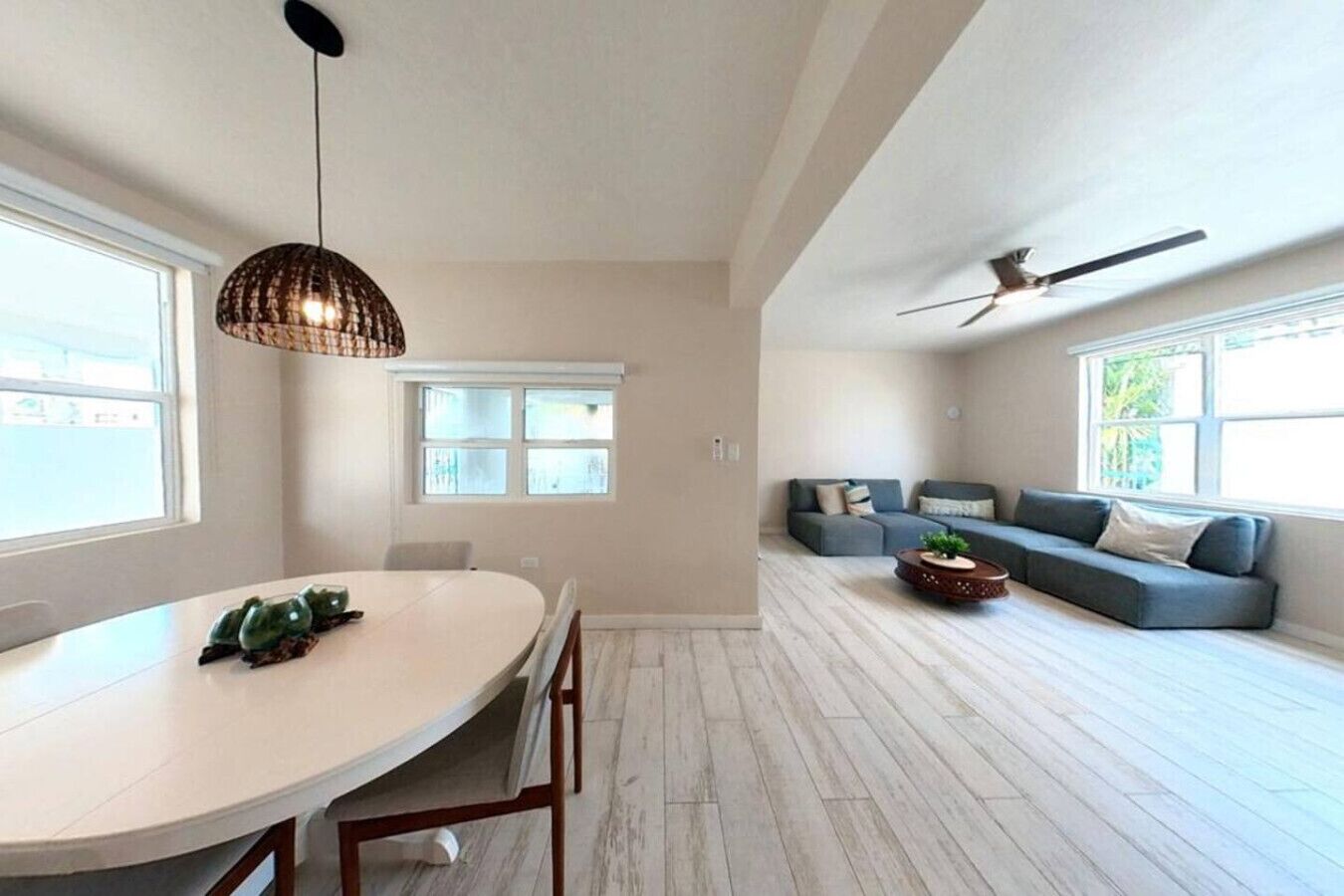 A spacious living area with a dining table, a sofa set, and a ceiling fan.