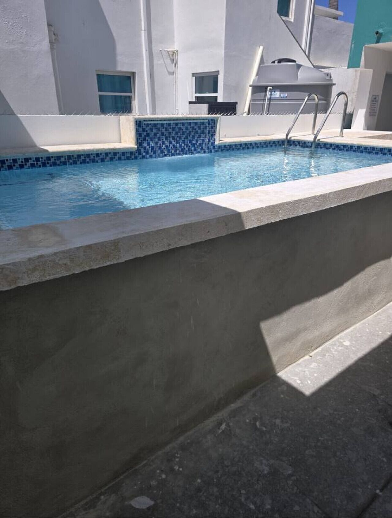 A swimming pool with a tiled edge, a concrete ledge, and a building with windows in the background.
