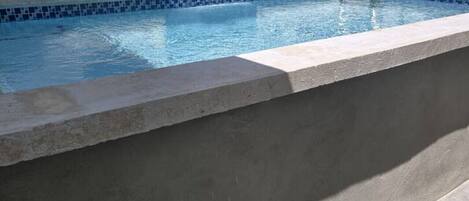 A swimming pool with a tiled edge, a concrete ledge, and a building with windows in the background.