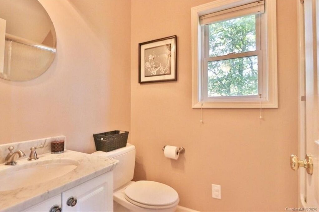 A bathroom with a white toilet, a sink with a marble countertop, a framed picture on the wall, and a window with a view of trees.
