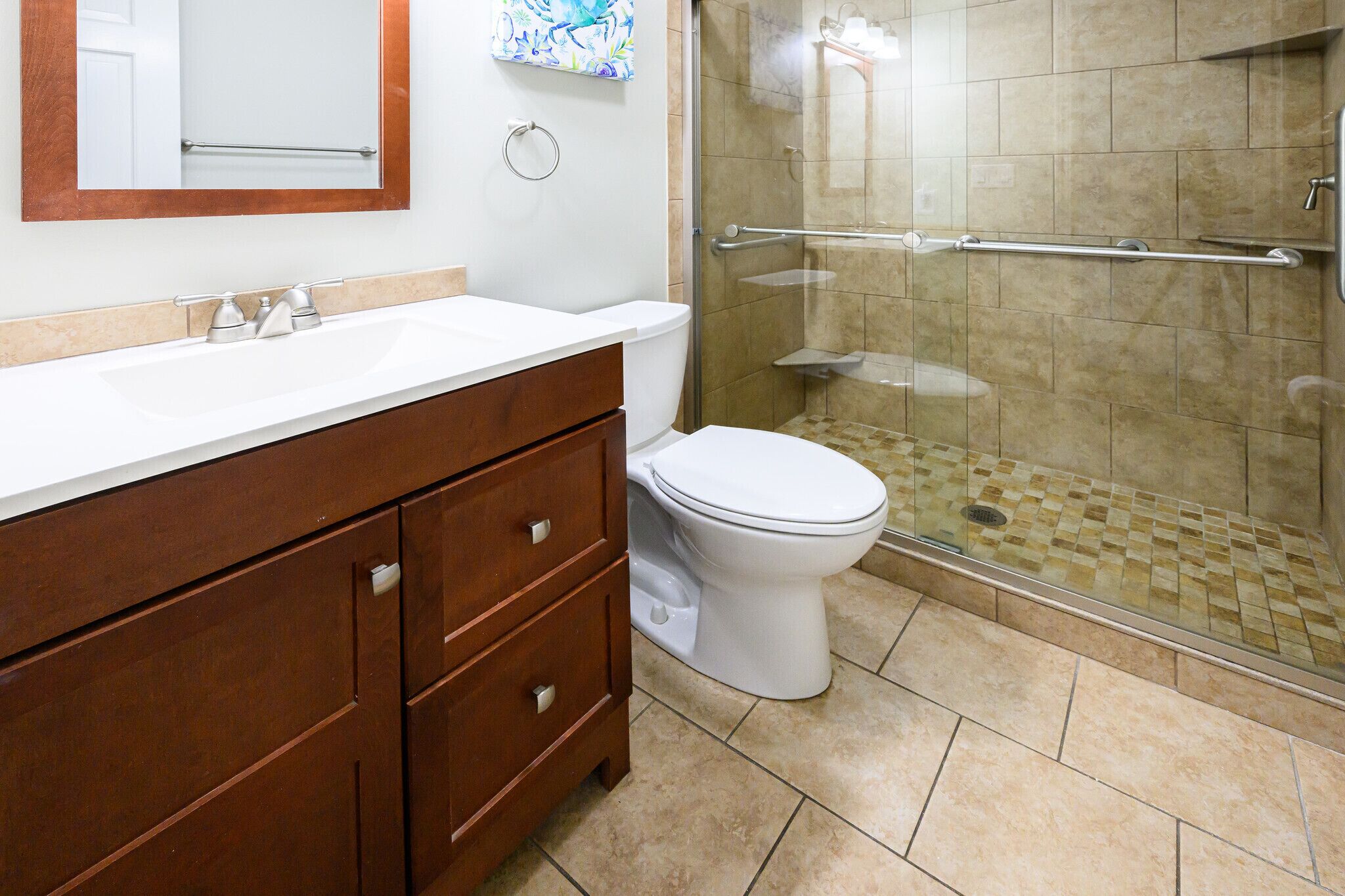 A bathroom with a white toilet, a wooden vanity with drawers, a glass shower enclosure, and a beige tiled floor.