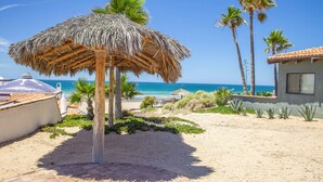 A beachside patio with a thatched umbrella, palm trees, and a view of the ocean.