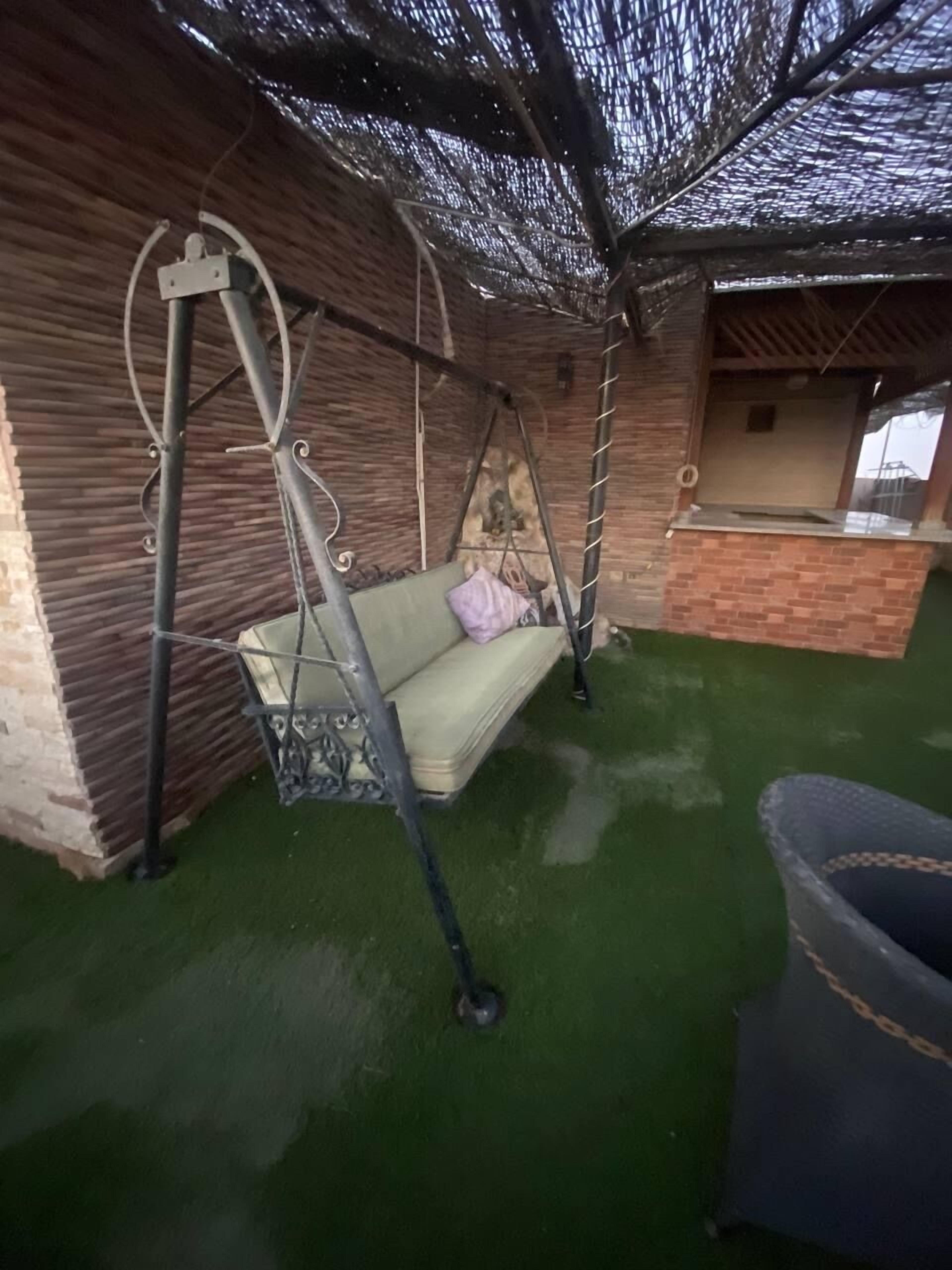 A room with a swing, a brick wall, a green artificial turf floor, and a window.