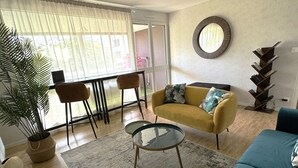 Una sala moderna con un sofá amarillo, un sofá azul, una mesa de centro de vidrio y un comedor con mesa y sillas.
