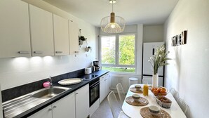 Una cocina moderna con armarios blancos, encimera negra y un comedor con mesa y sillas blancas.