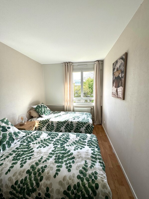 Un dormitorio con dos camas, una ventana con cortinas, un radiador y un cuadro en la pared.