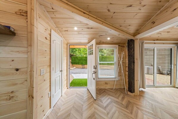 A wooden interior with a herringbone floor, a door leading outside, and a view of a garden.