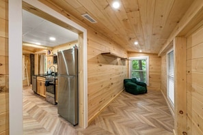 A wooden interior with a kitchen area, including a refrigerator and stove, and a herringbone-patterned floor.