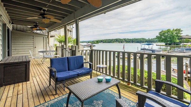A covered deck with a sofa, chairs, and a table, overlooking a body of water with boats. - Waterfront Condo Retreat in Garland County (Garland County)