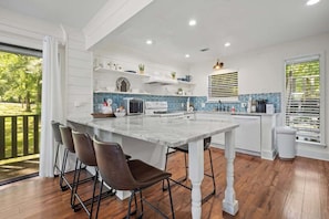 A modern kitchen with a large island, bar stools, and a view of the outdoors.