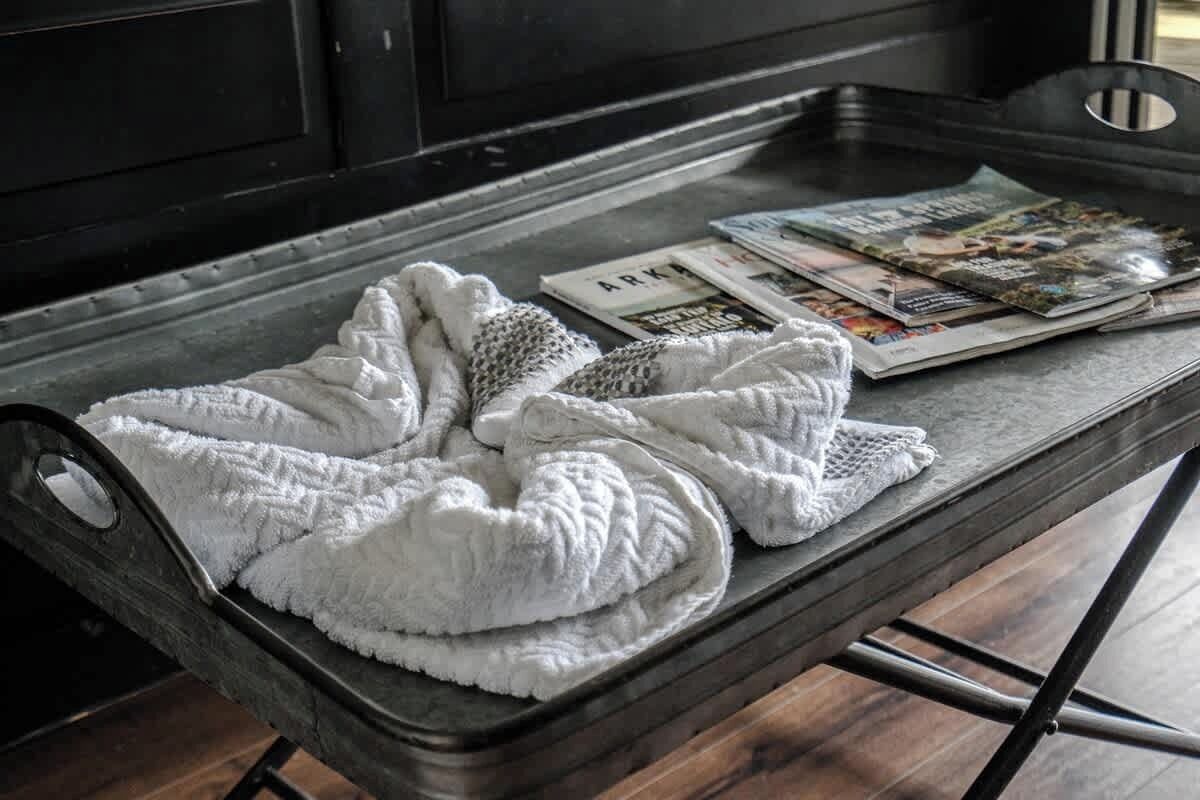 Una cama con una manta blanca y una revista sobre una bandeja de metal.