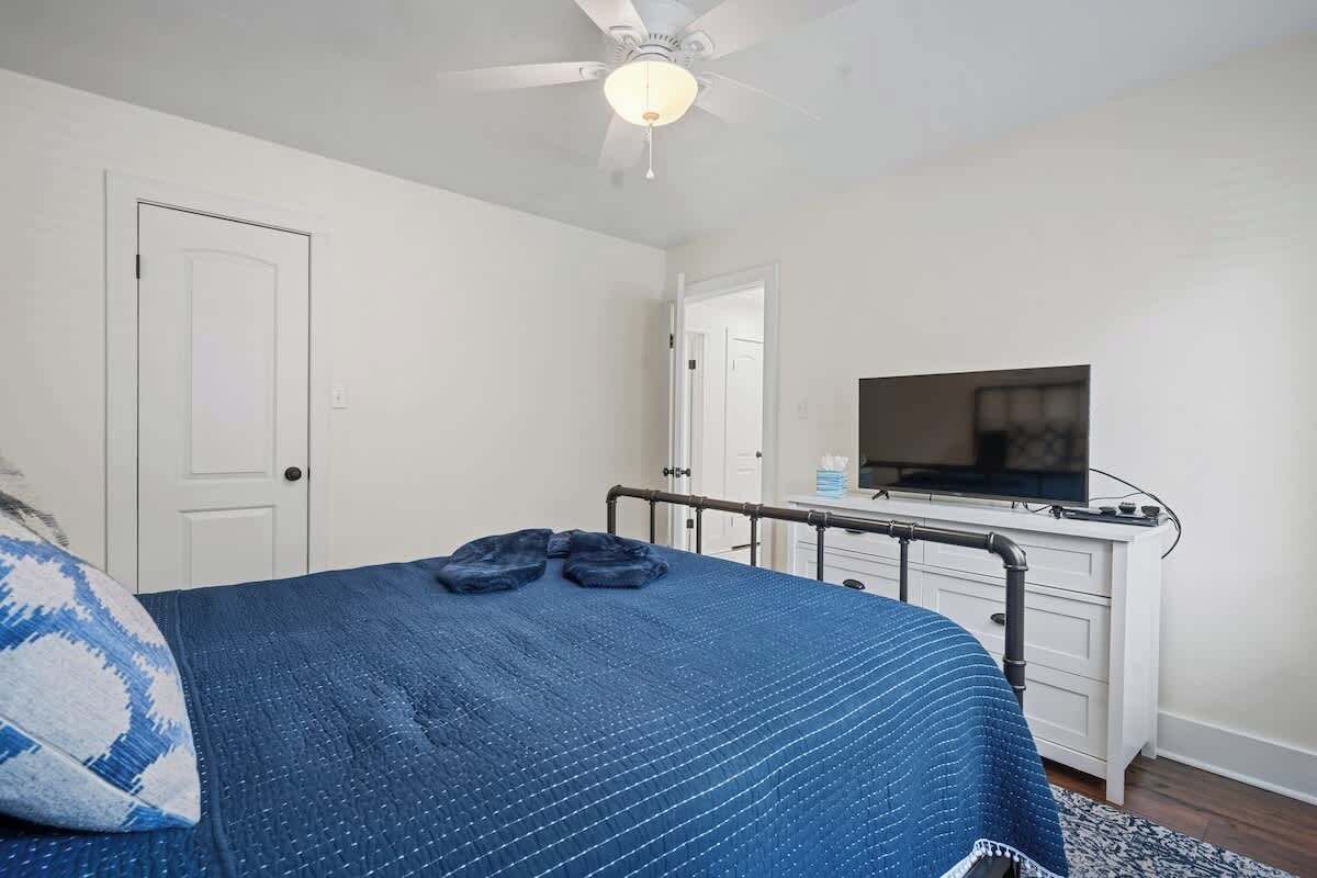 Une chambre à coucher avec un lit, un ventilateur de plafond, une télévision et une commode blanche.