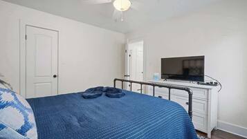 Une chambre à coucher avec un lit, un ventilateur de plafond, une télévision et une commode blanche.