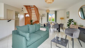 Una sala de estar moderna con un sofá verde, una zona de comedor, una escalera y una cocina.