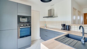 Una cocina moderna con gabinetes grises, horno empotrado, microondas, un lavamanos con grifo y una cafetera sobre la encimera.