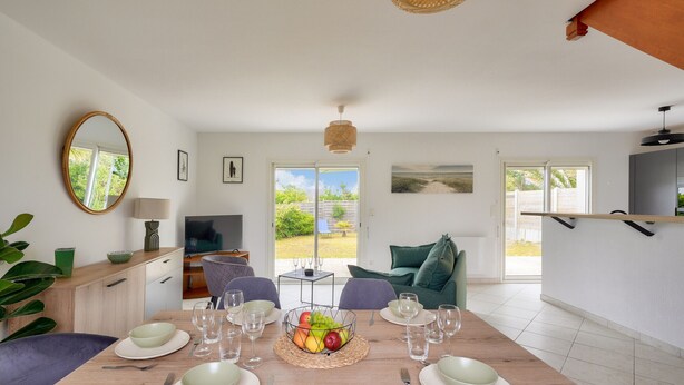 Un comedor con una mesa de madera dispuesta para cuatro, un frutero en el centro y vistas al exterior a través de amplias ventanas.