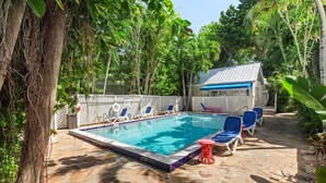 A swimming pool with stone tiles, surrounded by lounge chairs and a covered area with a blue roof. - Find your zen at HIDDEN TREASURE (Key West)