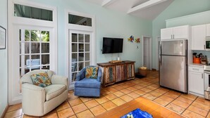 A spacious living area with a sofa, a blue armchair, a television, and a kitchen with a refrigerator and cabinets. - Find your zen at HIDDEN TREASURE (Key West)