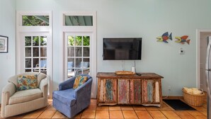 A living room with a beige armchair, a blue sofa, a wooden cabinet, a television, and two decorative fish wall art pieces. - Find your zen at HIDDEN TREASURE (Key West)