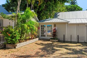 A small, single-story building with a metal roof, surrounded by lush greenery and a paved patio area. - Find your zen at HIDDEN TREASURE (Key West)