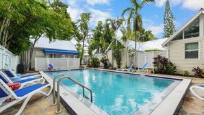 A swimming pool with lounge chairs, surrounded by palm trees and a stone patio. - Get your ISLAND STLYE on! (Key West)