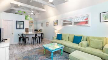 Un salon moderne avec un canapé vert, une table basse et un coin repas avec des chaises.