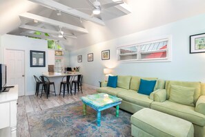 A modern living room with a green sofa, a coffee table, and a dining area with chairs. - Get your ISLAND STLYE on! (Key West)