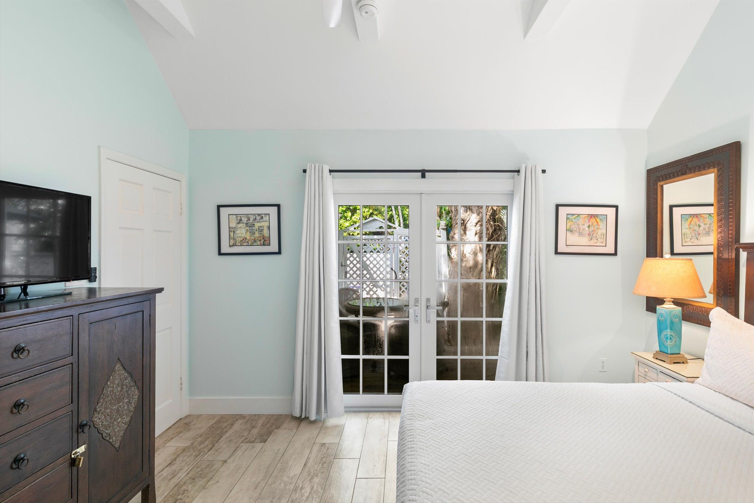 A bedroom with a bed, a television, a dresser, and a window with curtains.