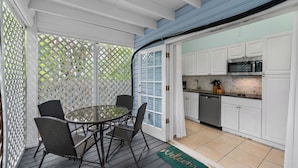 A covered patio with a round table and chairs, a kitchen with white cabinets and a microwave, and a welcome mat.