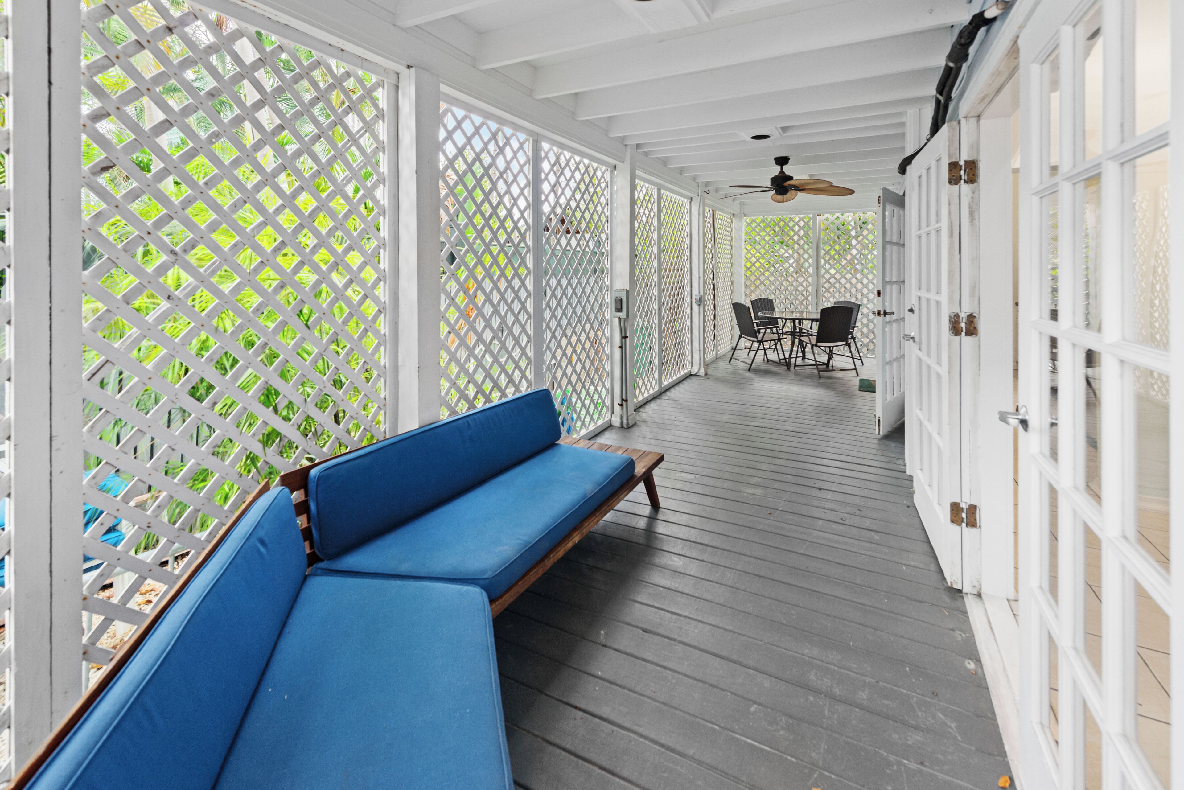 A covered porch with a blue bench, white lattice panels, and a dining area with chairs and a table.