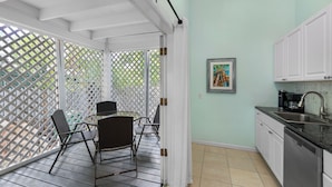 A covered patio with a dining table and chairs, a kitchen with white cabinets and a sink, and a door leading to an outdoor area with a lattice screen.