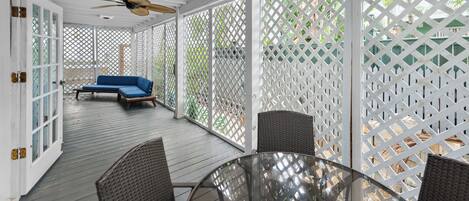 Un patio couvert avec une table en verre et des chaises en osier, un canapé bleu et un ventilateur de plafond.