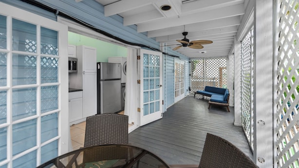 A covered outdoor area with a dining table and chairs, a ceiling fan, and a blue sofa.