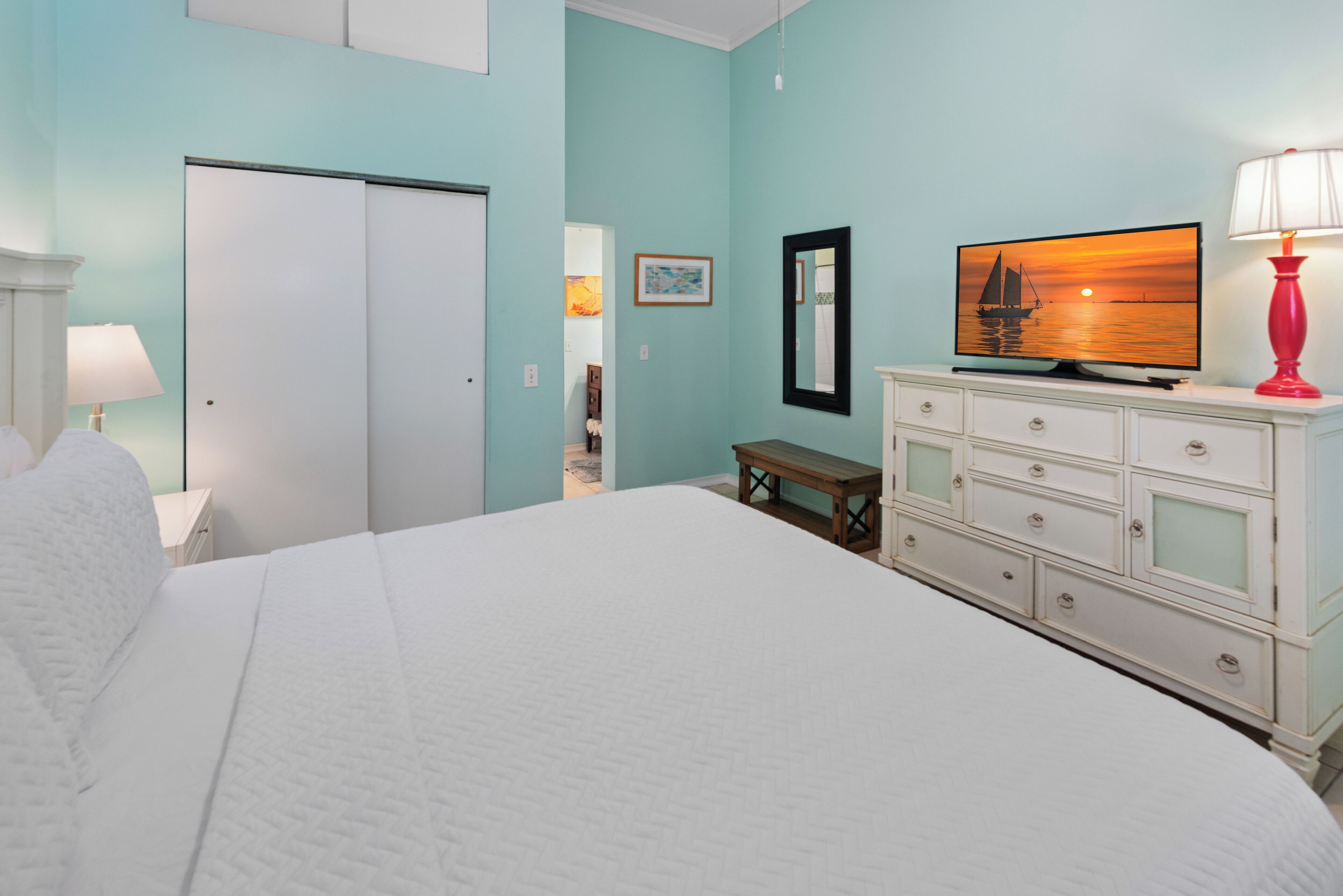 A bedroom with a bed, a dresser, a television, and a lamp.